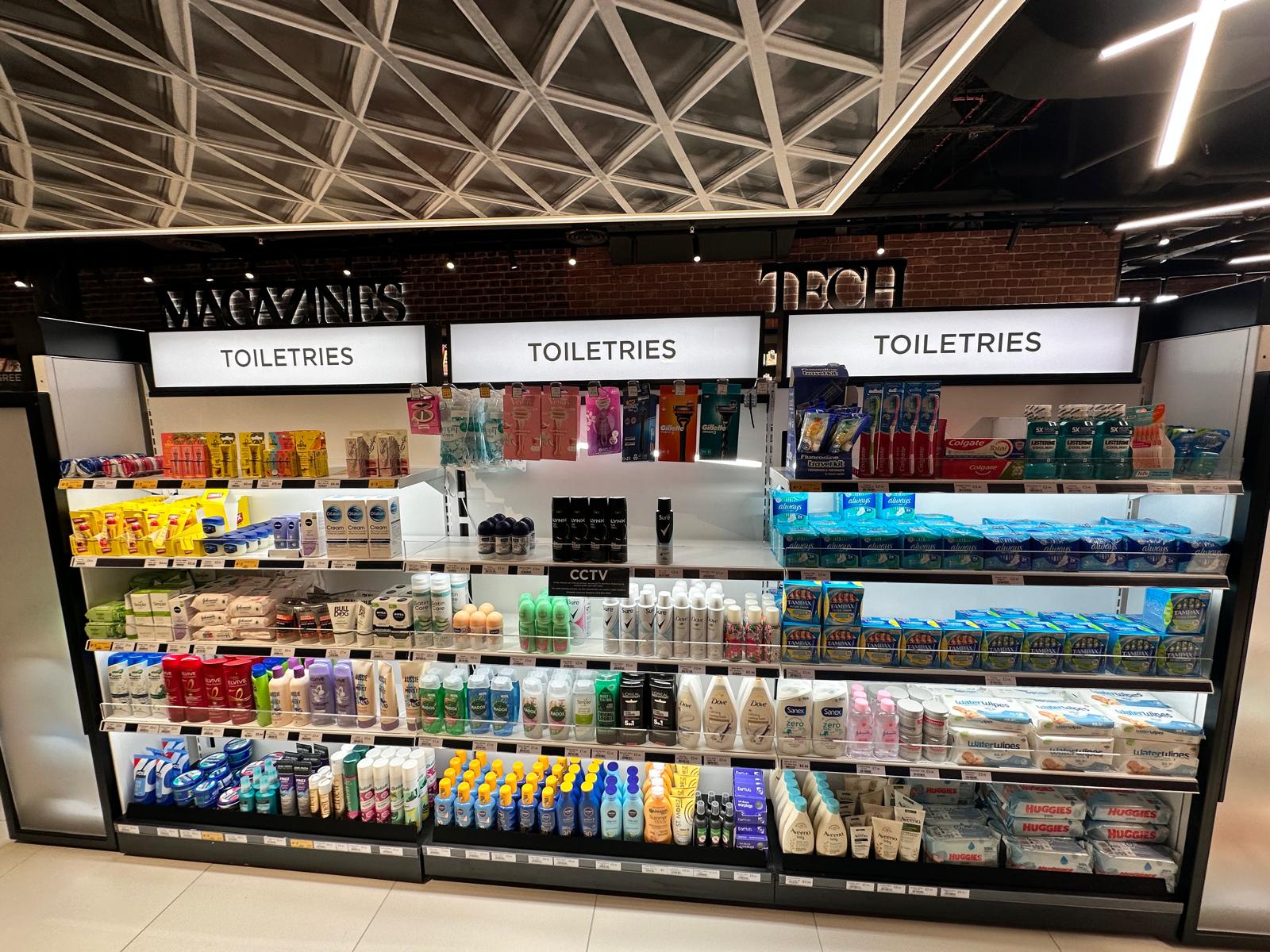 A well-lit store shelf labeled "Toiletries," displaying various personal care products such as soaps, shampoos, toothpaste, deodorants, and sanitary products arranged neatly in multiple rows.