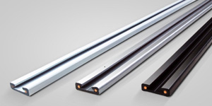 Three metal U-channel strips are shown on a light background. Two are silver and one is black. Each channel contains copper-colored circular elements inside the groove.
