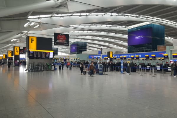 A spacious and modern airport terminal with high ceilings and a bright, open layout. Large display boards with flight information and yellow section signs (E and F) are visible. Passengers are lining up at check-in counters with blue and yellow signage, guided by sleek LED wayfinders.