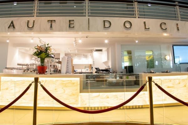 A brightly lit, modern café named "Haute Dolci" with elegant white and gold decor. The counter features an LED Light Sheet panel to create backlit art in a stunning marble pattern.