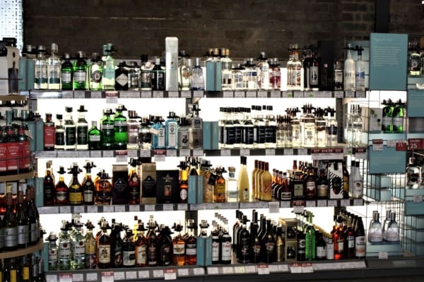 A well-stocked liquor store shelf displaying a variety of alcoholic beverages, including wine, gin, whiskey, vodka, and other spirits. The bottles are neatly arranged and illuminated by an LED light sheet panel with price labels visible on the shelves.
