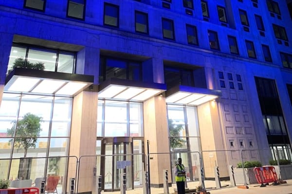 A modern building facade at night, featuring large, illuminated windows and futuristic canopy lights above the entrances. The Shell Centre building's exterior is bathed in a blue light, highlighting its clean lines and contemporary architectural style.