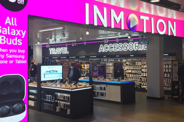 A brightly lit InMotion store features a backlit graphic with a large sign offering "15% off All Galaxy Buds when you buy any Samsung Phone or Tablet." The store showcases various electronic gadgets and accessories, with several customers browsing inside.