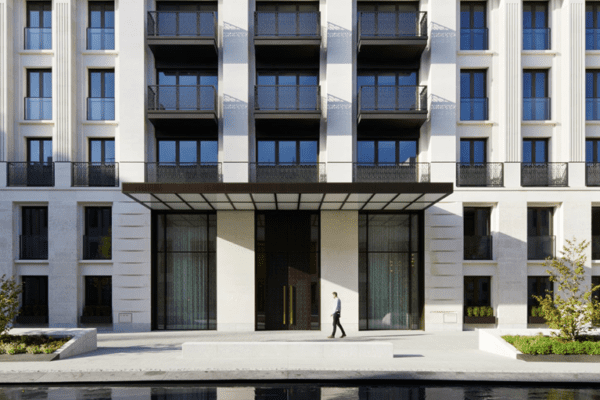 An outdoor entrance with a backlit canopy illuminated by Bright Green Matrix lighting. The canopy's structured design casts a warm glow over the entrance, which features large glass panels and sleek black double doors. The surrounding facade consists of white stone with clean lines, complementing the modern and inviting aesthetic.