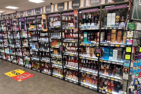 Morrison's store display showcases champagne and sparkling wine, each marked with a price tag. Under the cheerful sign "Buzz for booze!" LED light panels at 6500K illuminate the selection with brilliance as a button uses electromagnetic locks to prevent theft.