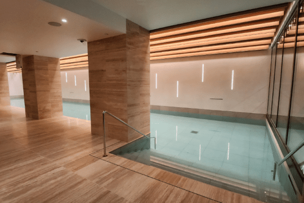 A modern indoor swimming pool with clean lines and minimalist design, enhanced by a Bright Green Grid system. The ambient lighting and wooden paneling create a luxurious feel, while marble walls add elegance. Dynamic White panels adjust color temperature perfectly to this serene environment.