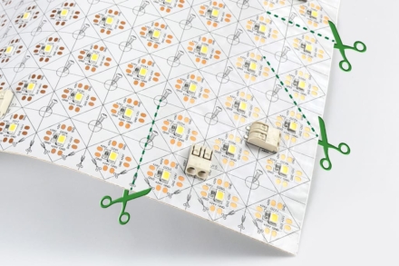 A patterned sheet of Bright Green GridFlex with electronic components and dotted green lines indicating where to cut, marked by green scissor icons. Two small beige connector pieces rest on top of the sheet.