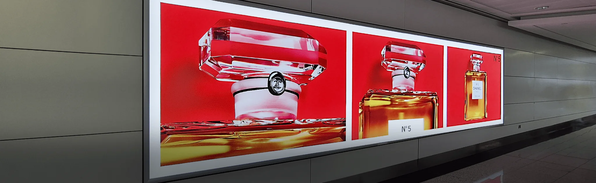 An advertisement in a hallway shows two images of perfume bottles with red backgrounds. The left image highlights the bottle's top, and the right image displays the full bottle with the label "N°5." The setting appears modern and sleek.