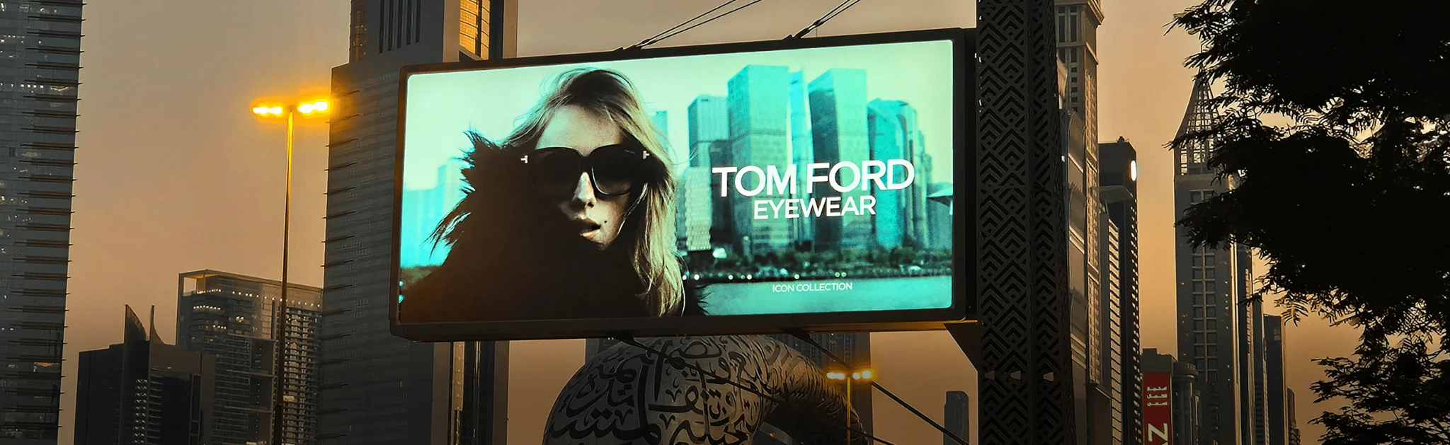 Billboard featuring a woman in large sunglasses, promoting "Tom Ford Eyewear" against a backdrop of modern skyscrapers at sunset.